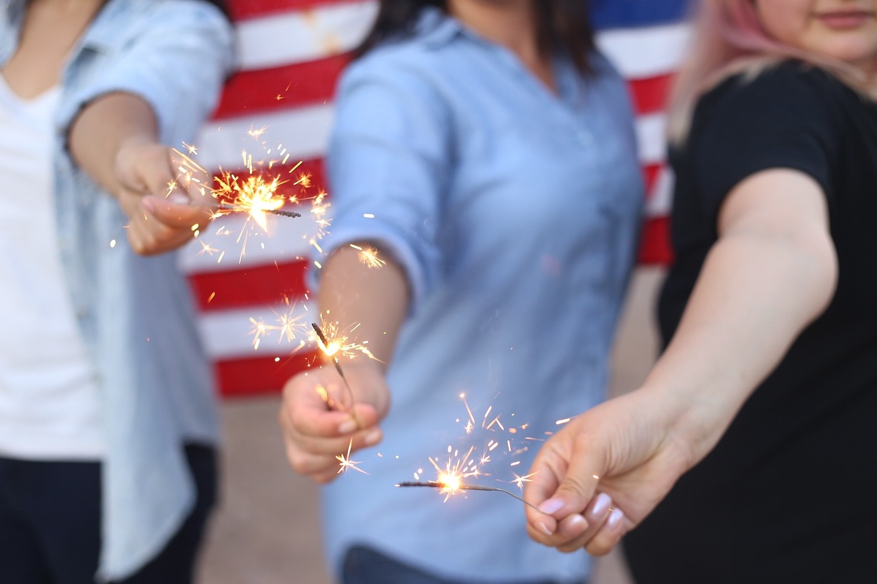 Three people holding sparklers with an American flag in the background during a hood river 4th of july celebration